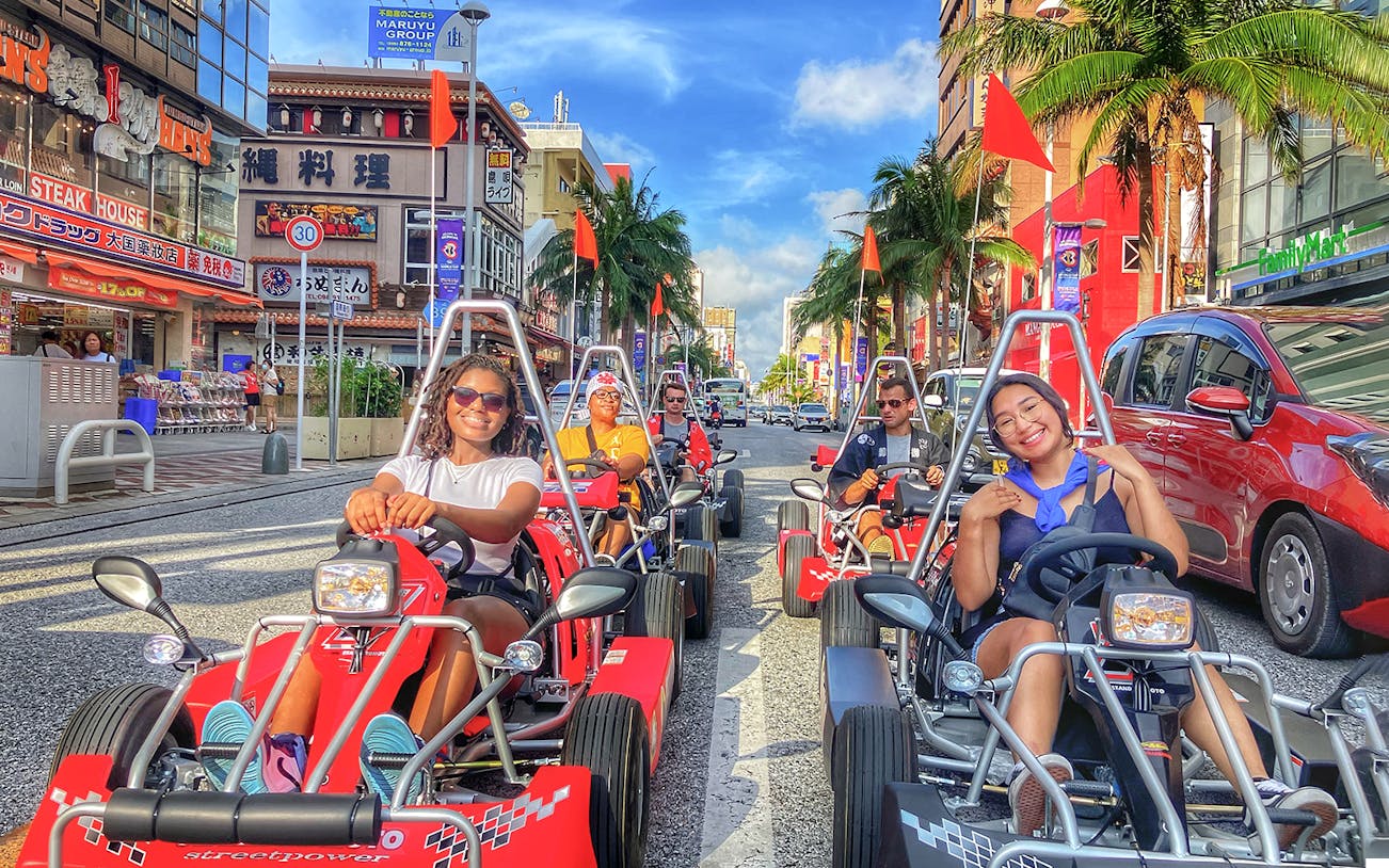 Go-karting on a busy street in Okinawa with palm trees and shops in the background.