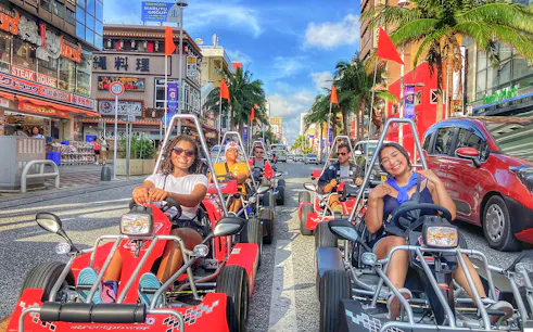 Go-karting on a busy street in Okinawa with palm trees and shops in the background.