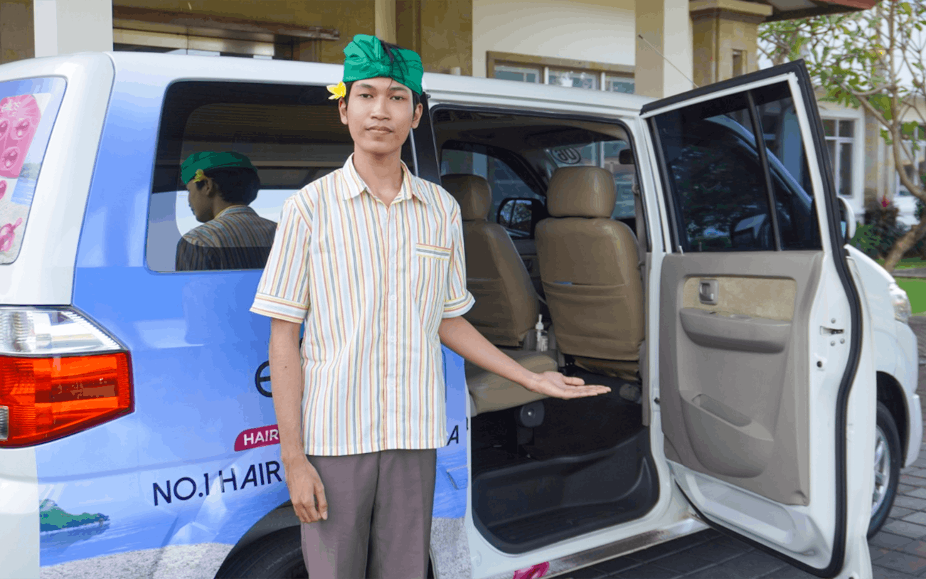 Man welcoming passengers to a van for shared airport transfers from Bali International Airport.