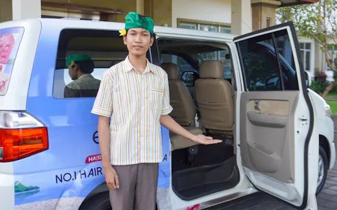 Man welcoming passengers to a van for shared airport transfers from Bali International Airport.