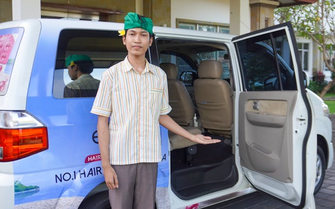 Man welcoming passengers to a van for shared airport transfers from Bali International Airport.