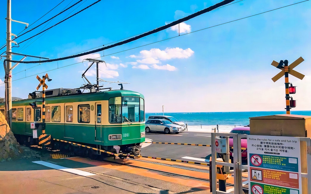 Enoshima railway train crossing near the ocean with cars in the background.