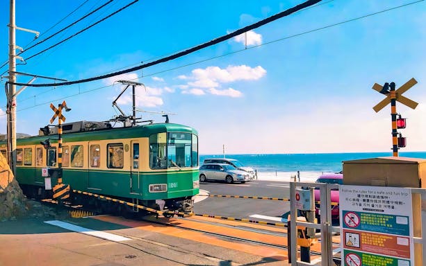 Enoshima railway train crossing near the ocean with cars in the background.