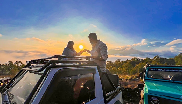 Two people enjoying sunrise from a jeep on Mount Batur, Bali, with scenic views.
