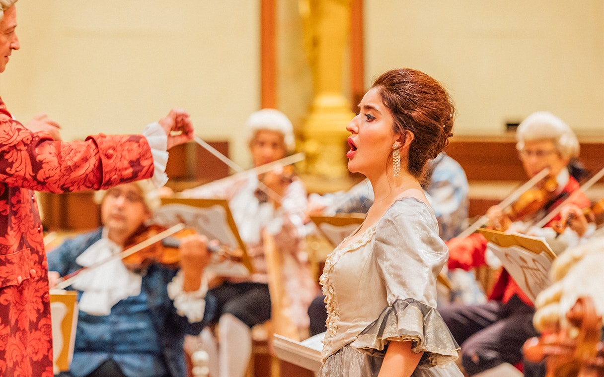 Vienna State Opera performance with singer and orchestra in period costumes.