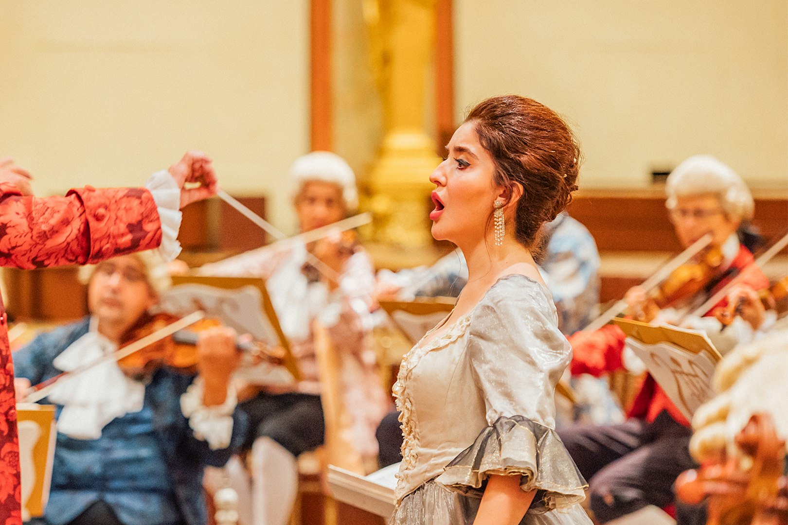 Vienna State Opera performance with singer and orchestra in period costumes.
