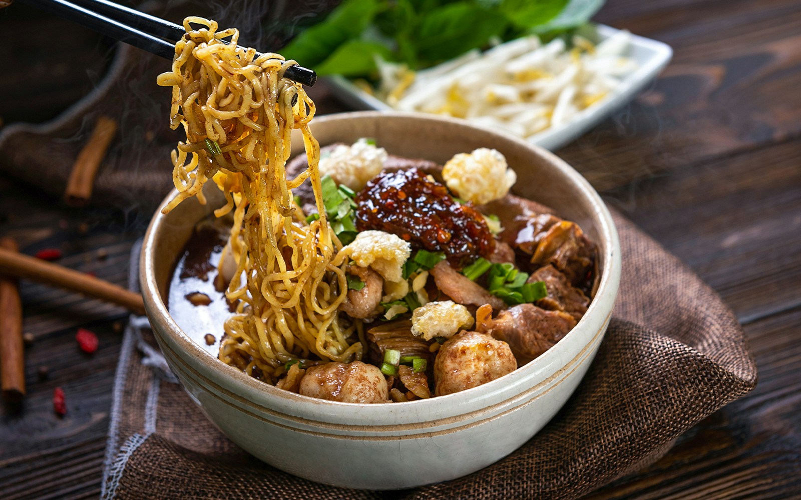 Bowl of Asian noodles with meat, vegetables, and sauce, served with chopsticks.