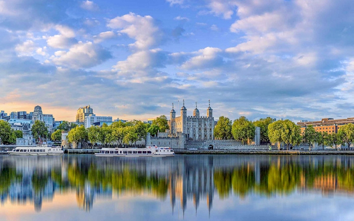 Tower of London viewed from a Thames River cruise with cityscape backdrop.