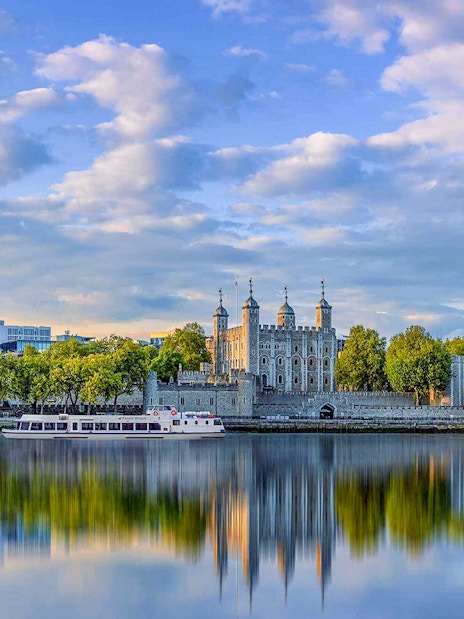 Tower of London viewed from a Thames River cruise with cityscape backdrop.