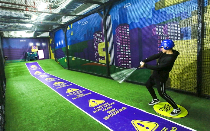 Man practicing baseball in a netted area at SuperPark Singapore.