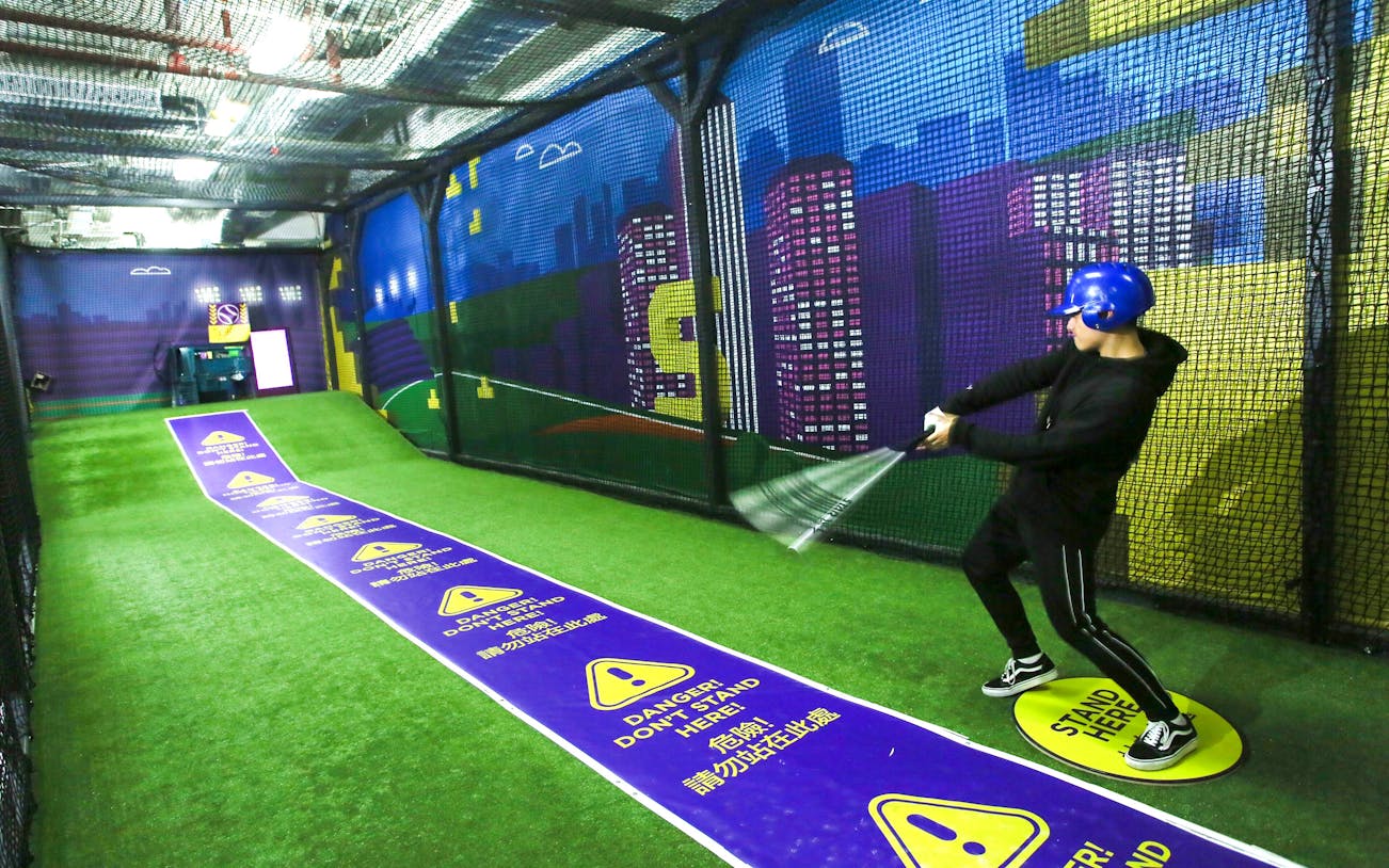 Man practicing baseball in a netted area at SuperPark Singapore.