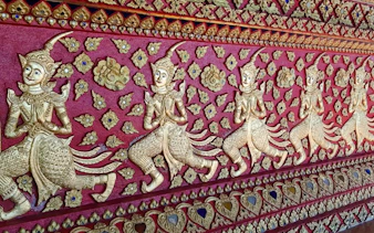 Golden carvings on a red temple wall in Chiang Mai, featuring intricate mythical figures.