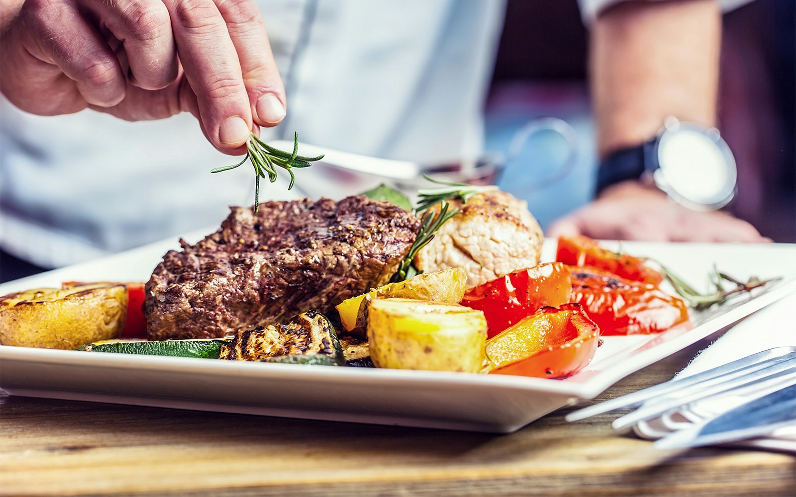 Chef garnishing steak with rosemary, served with grilled vegetables near Umeda Sky Building.