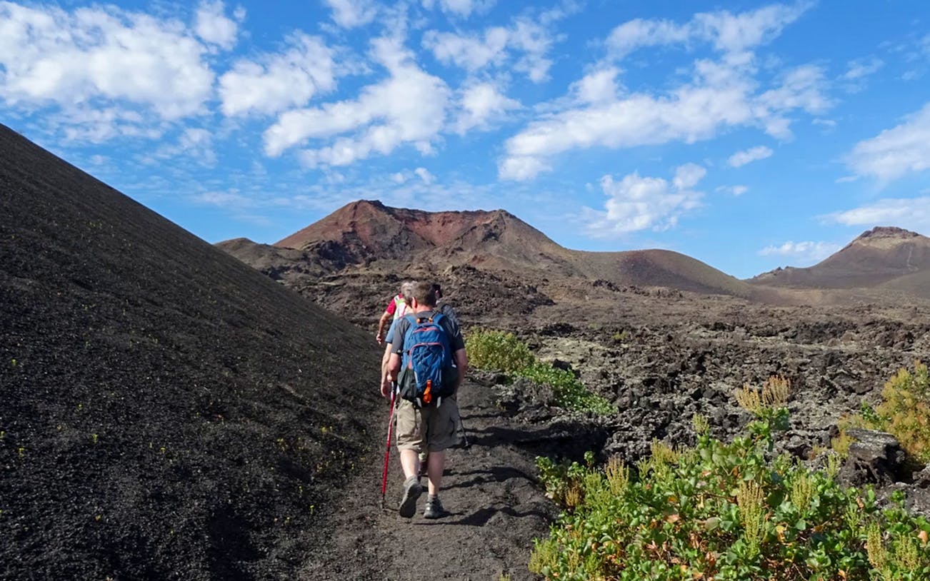 Hikers on a trail through volcanic terrain at Timanfaya National Park, Lanzarote.