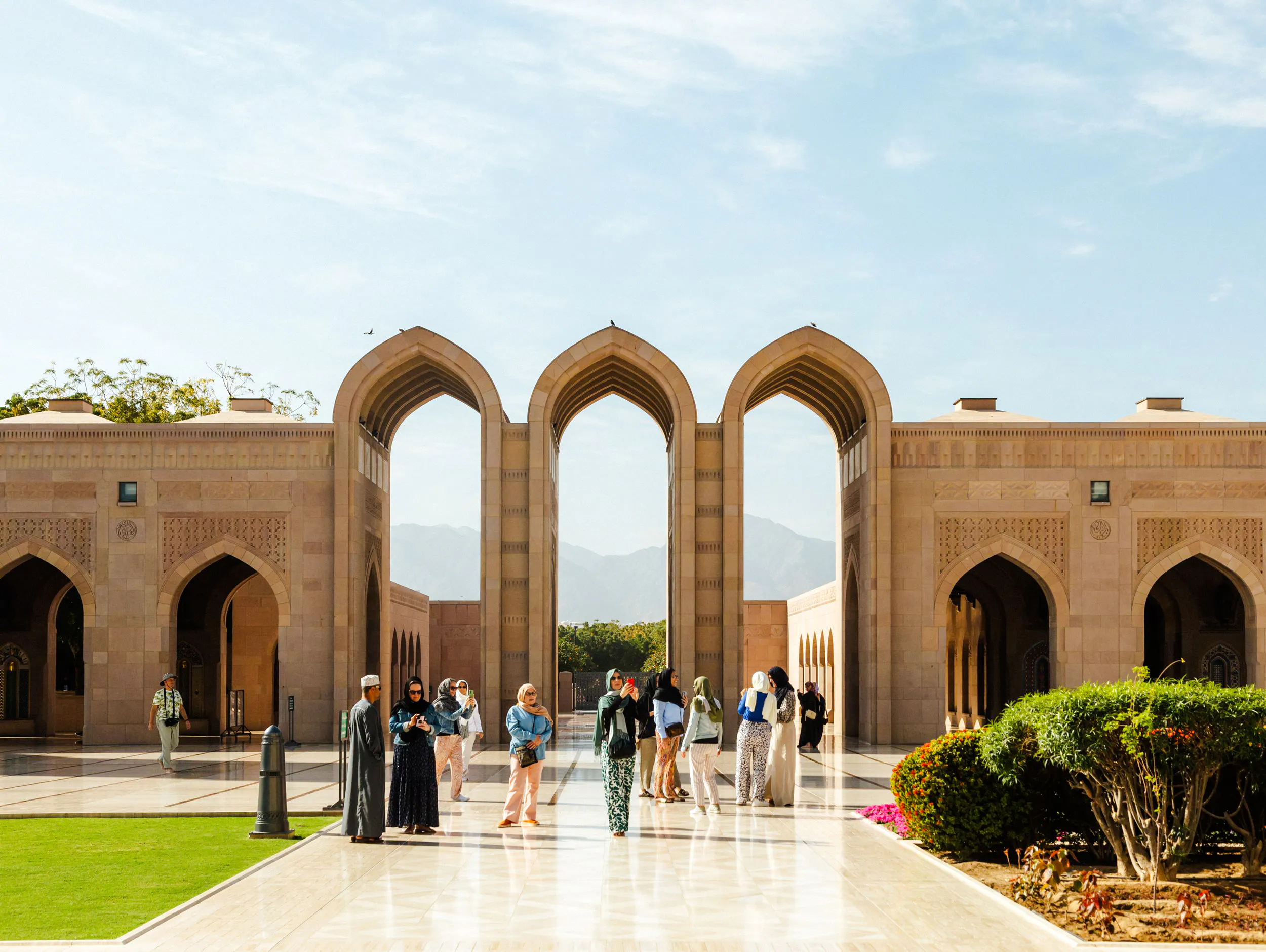 Visitors exploring the Sultan Qaboos Grand Mosque courtyard in Muscat.