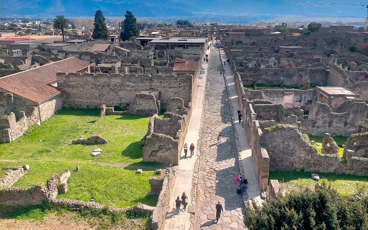 Ancient ruins and cobblestone street in Pompeii, Italy, with tourists exploring the site.