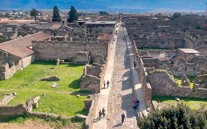 Ancient ruins and cobblestone street in Pompeii, Italy, with tourists exploring the site.