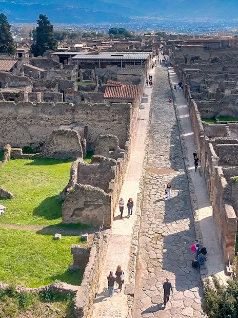 Ancient ruins and cobblestone street in Pompeii, Italy, with tourists exploring the site.