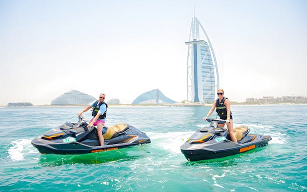 Two people jet skiing in Dubai with Burj Al Arab in the background.