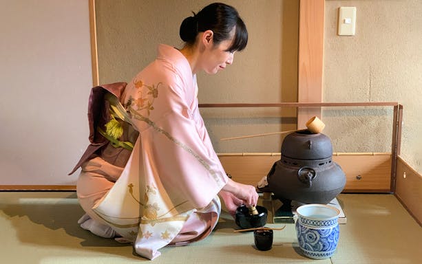 Tea ceremony in Kyoto teahouse with woman in kimono preparing tea.