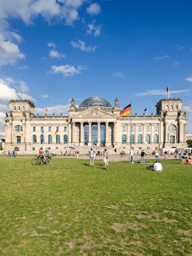 Reichstag building in Berlin with visitors on the lawn, featuring its iconic glass dome.