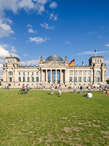 Reichstag building in Berlin with visitors on the lawn, featuring its iconic glass dome.