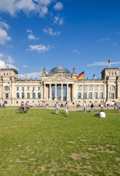 Reichstag building in Berlin with visitors on the lawn, featuring its iconic glass dome.