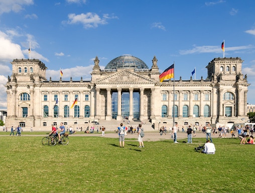 Reichstag building in Berlin with visitors on the lawn, featuring its iconic glass dome.