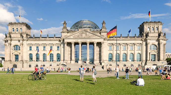 Reichstag building in Berlin with visitors on the lawn, featuring its iconic glass dome.