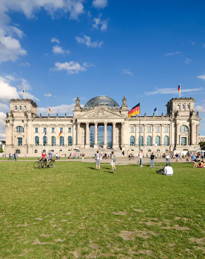 Reichstag building in Berlin with visitors on the lawn, featuring its iconic glass dome.