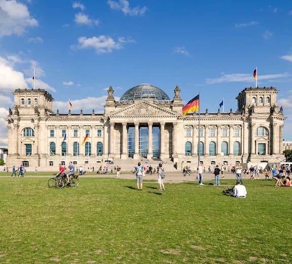 Reichstag building in Berlin with visitors on the lawn, featuring its iconic glass dome.