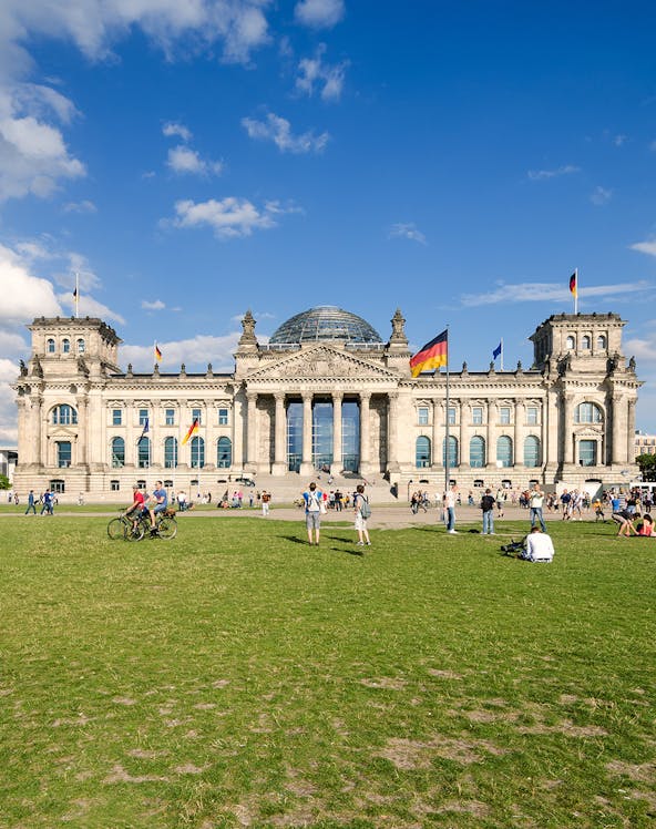 Reichstag building in Berlin with visitors on the lawn, featuring its iconic glass dome.