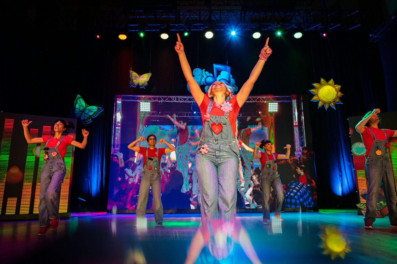 Performers on stage during Cantajuegos 20 Años show with colorful lights and decorations.