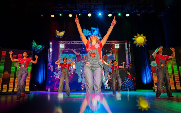 Performers on stage during Cantajuegos 20 Años show with colorful lights and decorations.