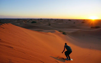 Sandboarding at sunset on Sahara Desert dunes.
