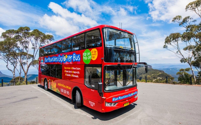 Red double-decker bus for Blue Mountains Hop-On Hop-Off Tour with scenic views in background.