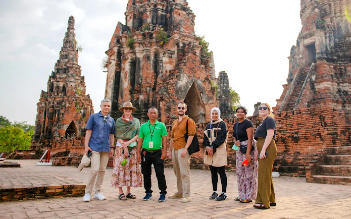Tourists with guide at Wat Chaiwatthanaram, Ayutthaya, standing in front of ancient temple ruins.