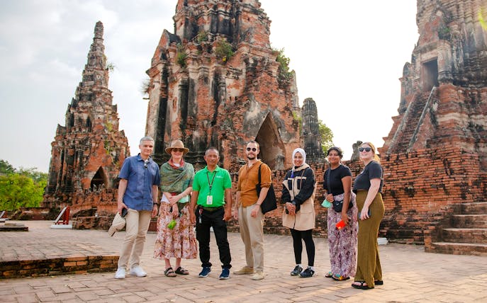 Tourists with guide at Wat Chaiwatthanaram, Ayutthaya, standing in front of ancient temple ruins.