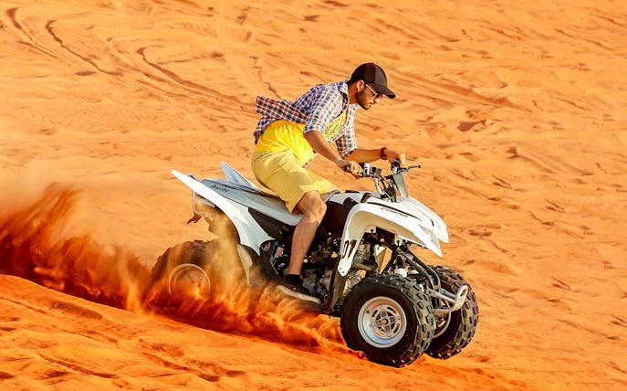 Quad biking on desert dunes during adventure tour.