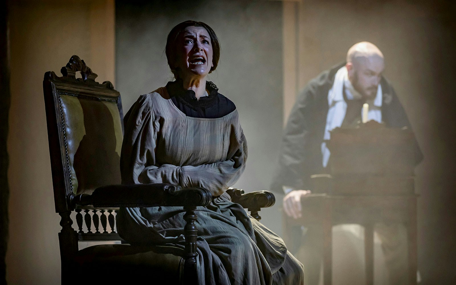 Woman in period costume sitting in a chair, with a man in the background, related to Mrs President.
