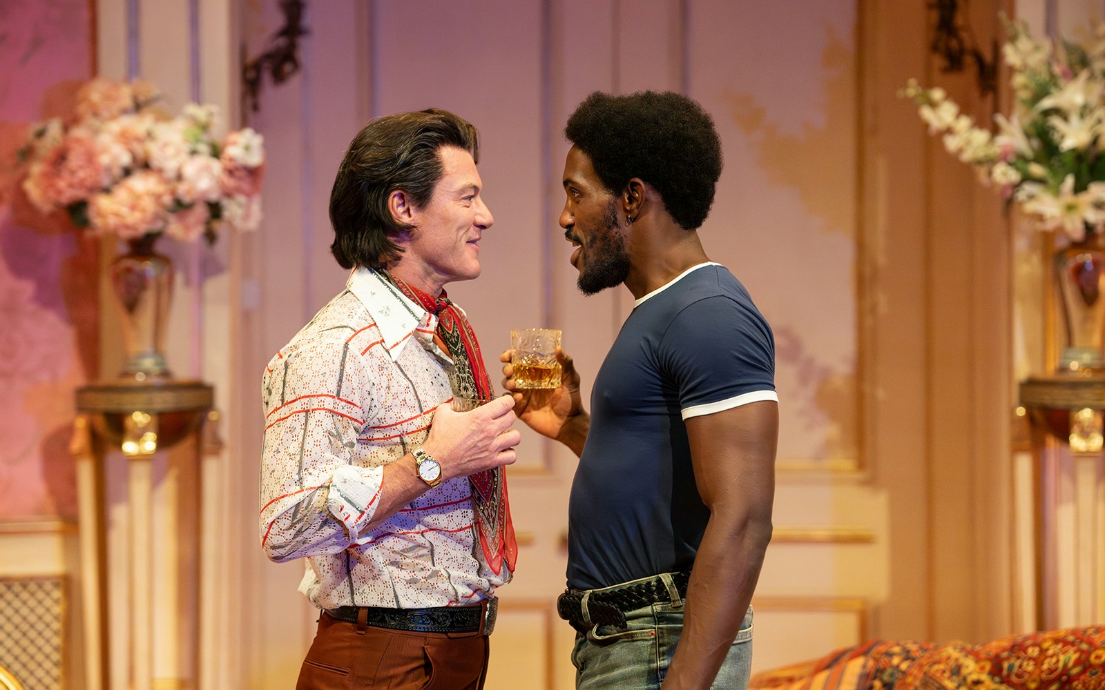 Two actors in a theatrical scene from "Backstairs Billy," holding drinks and conversing.