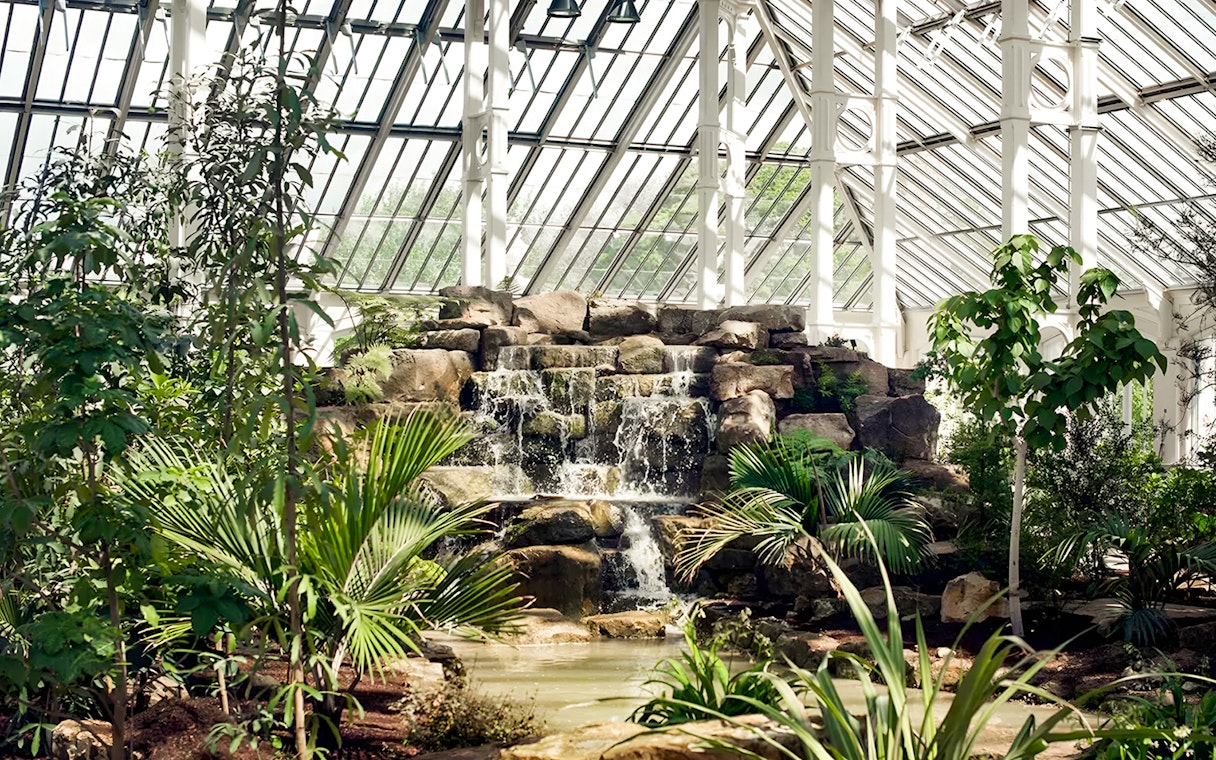 Waterfall and lush greenery inside Kew Gardens' glasshouse, London.