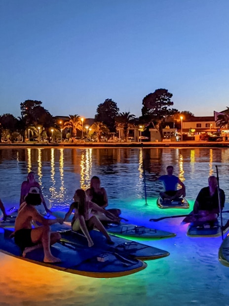 Paddleboarders on illuminated boards during SUP Glow Tour in Split at dusk.