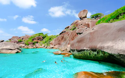 Snorkelers in clear turquoise water near rocky Similan Islands, Krabi, with lush greenery.