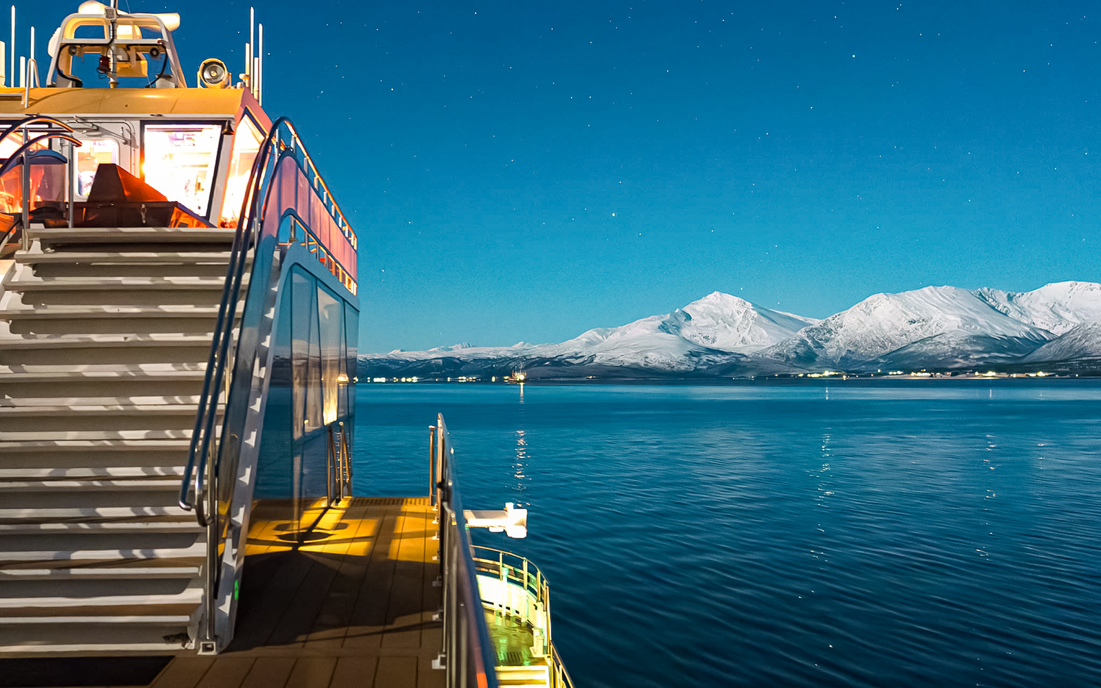 Cruise ship deck with snowy mountains under starry sky, Aurora Boreal dinner cruise.