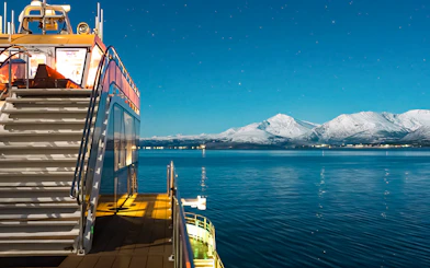 Cruise ship deck with snowy mountains under starry sky, Aurora Boreal dinner cruise.