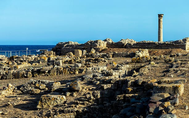 Nora Archaeological Site ruins with ancient column and sea view in Sardinia.