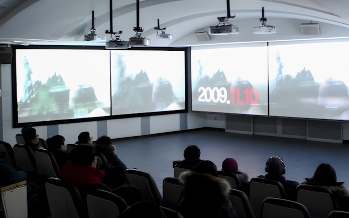 Audience watching a DMZ Tour presentation in a theater setting.
