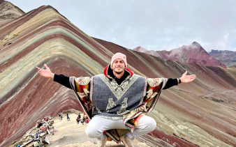 Person posing in front of Rainbow Mountain, Cusco, with colorful striped terrain.