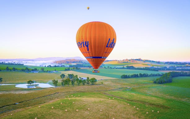 Hot air balloon floating over Yaara Valley landscape with fields and hills.